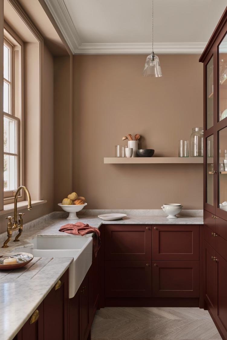 A traditional kitchen from Paint & Paper showing brown cabinetry, light brown walls, a dark brown dresser with a marble kitchen worktop and copper tap