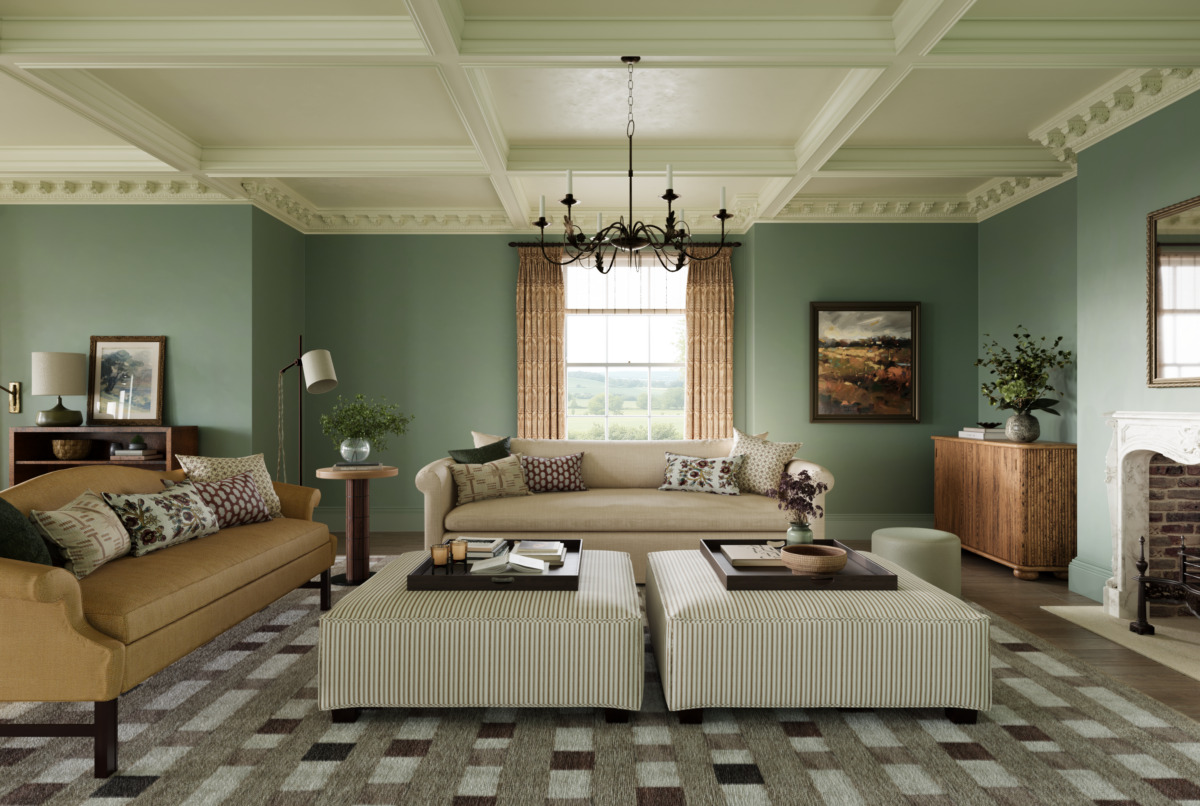 A wide shot of the The ground floor floor plan of the Sussex Estate Interior Design project drawing room showing two large sofas with two large footrests in the middle. Surrounding the room are olive green walls, a white panelled ceiling and marble fireplace.