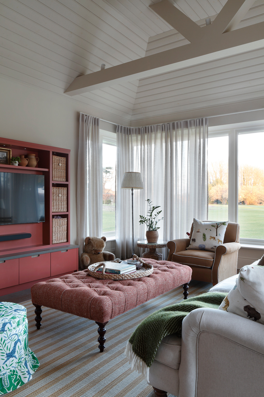 A side view of a large bright luxury childrens playroom in the West Sussex House interior design project with sofas, armchairs, TV cabinet and pouffe. A teddy bear is in the background.