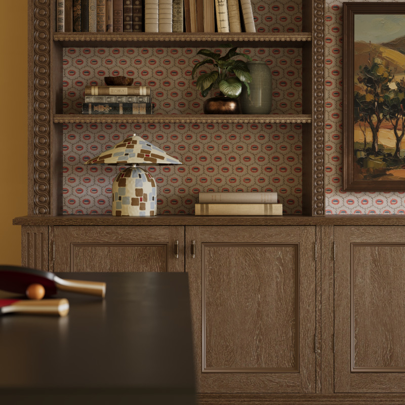 A solid wood bookcase with wallpaper back sits behind a table tennis table in the Sussex estate house. On the shelves are a variety of books, plants and a small danish inspired table lamp.