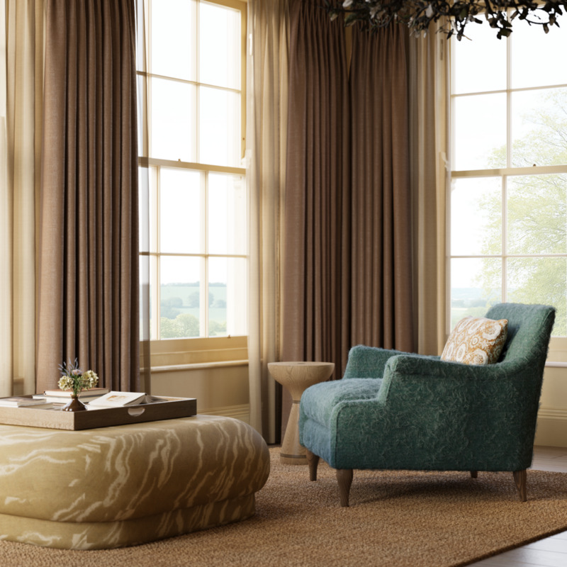 Sunlit living interior design room with teal armchair, patterned ottoman, wooden tray, books, and flowers, beside tall windows with layered curtains, overlooking through sash windows a serene English country landscape and anchored by a textured rug from Studio Hooton of Mayfair.