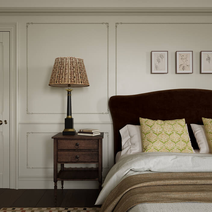 A close up view of the bed and bedside table of the Queen Anne Interior Design Project showing a sumptuous bed with dark green fabric headboard, an antique hardwood bedside table on which sits a tall table lamp with floral lampshade.