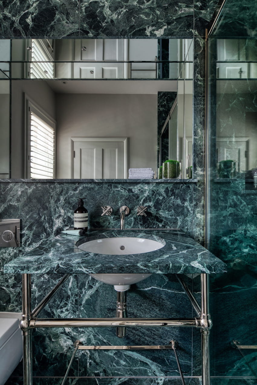 A green marbled wash basin with chrome legs sits aside a matching green marbled wall and large flat rectangular mirror. To demonstrate the bathroom design of Studio Hooton's interior design services.