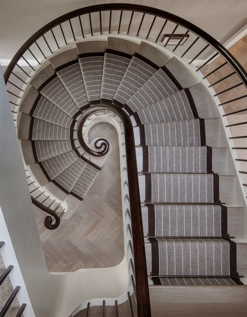 An aerial view of an elegant curved Georgian staircase with dark wood bannister and grey and brown stair runner. Used for interior architecture, part of Studio Hooton's interior design services.