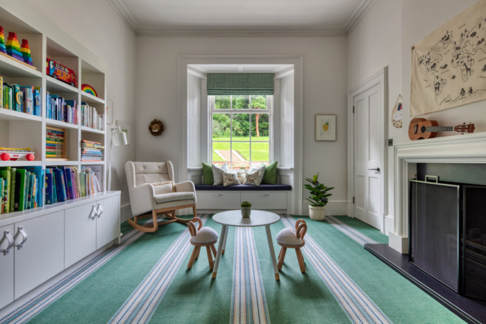 A luxury childrens playroom with armchair, table and chairs, storage for books and toys on a striking green carpet