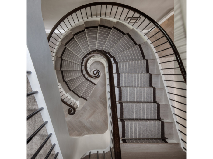 Aerial view of a luxurious spiral staircase. Dark hardwood bannisters with a striped grey and dark brown edging carpet.
