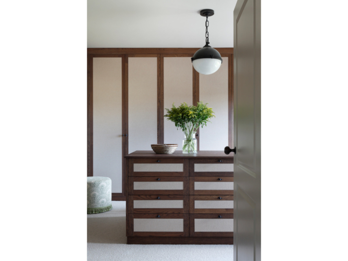 A freestanding chest of drawers with rich wood veneer stands in the center of the room behind a series of cupboards which are identically designed. The headline image for an article about illuminating your home.
