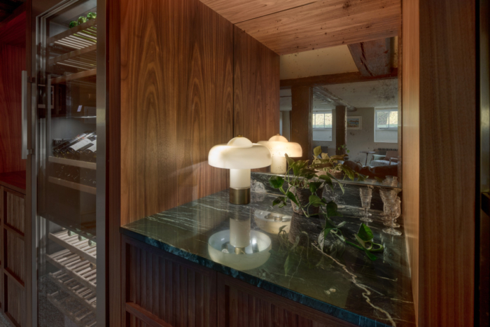 A luxury green marble worktop sits next to a large hardwood encased wine cooler. On the worktop sits a lit white and gold art deco inspired modern table lamp to showcase the electronic automation provided by Tillman Domotics.